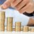 Hand placing a coin on a stack of coins, symbolizing financial savings and cost reduction strategies for homeowners.