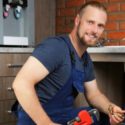 Plumber working under a kitchen sink, demonstrating plumbing repair and maintenance techniques relevant to home plumbing services.