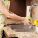 Person cleaning a kitchen sink with stone countertop, highlighting kitchen plumbing and maintenance.