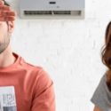 Frustrated man and woman sitting indoors under an air conditioning unit, illustrating discomfort from insufficient cooling in a home.