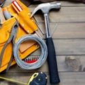 Tools on a wooden surface, including a hammer, nail puller, and tape measure, representing home maintenance and repair.