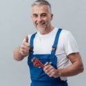 Plumber in blue overalls giving a thumbs-up while holding a wrench, representing expert plumbing services by Laney’s Inc.