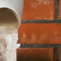 Drain pipe with flowing water on a textured brick floor, highlighting potential plumbing issues for homeowners.