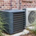 Air conditioning units against a brick wall, featuring a dark gray compressor and lighter condenser for optimal home comfort.
