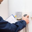 Technician in blue uniform adjusting a thermostat for Laney's Inc. home maintenance services.