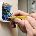 Person installing a thermostat with a yellow screwdriver, showcasing HVAC maintenance and home service by Laney's Inc.