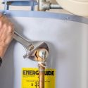Hand using an adjustable wrench on a water heater with copper piping, showcasing Laney's Inc. home maintenance expertise.