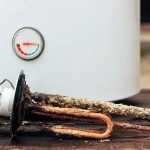Water heater maintenance components, including a corroded heating element and temperature gauge, emphasizing the importance of upkeep for energy efficiency and performance.