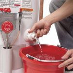 Person performing maintenance on a water heater, pouring water into a red bucket, demonstrating essential upkeep for improved energy efficiency and performance.