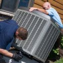 Technicians in uniforms install an outdoor air conditioning unit, showcasing HVAC maintenance for homeowners.
