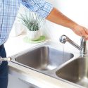 Person using a kitchen faucet to demonstrate plumbing services related to drain cleaning and maintenance.