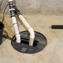 Sump pump system setup with plastic tubes, pump, and bucket for effective home water management.