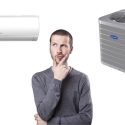 Person contemplating between ductless and central air conditioning systems, with a ductless unit on the left and a central AC unit on the right, related to home HVAC installation options.
