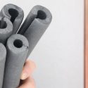 Human hand gripping dark gray foam tubes for home maintenance tasks related to plumbing and HVAC services at Laney's Inc.