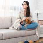 Young woman knitting on a sofa with yarn, enjoying natural light in a cozy home, representing Laney's Inc home services.