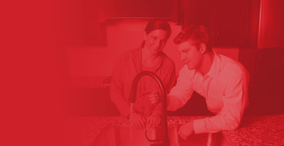 Man and woman discussing plumbing solutions at a kitchen sink, emphasizing customer service and home comfort in HVAC and plumbing contexts.