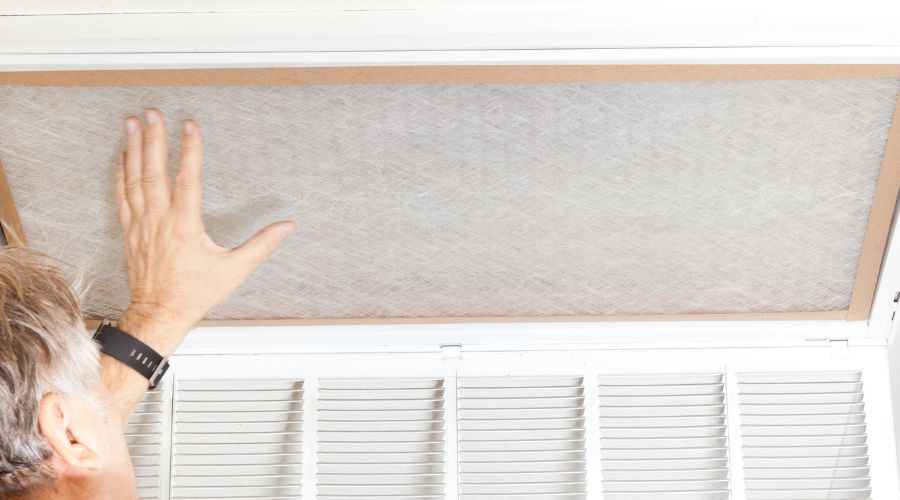 Person replacing air filter in HVAC system, emphasizing importance of air quality and maintenance for efficient heating and cooling.